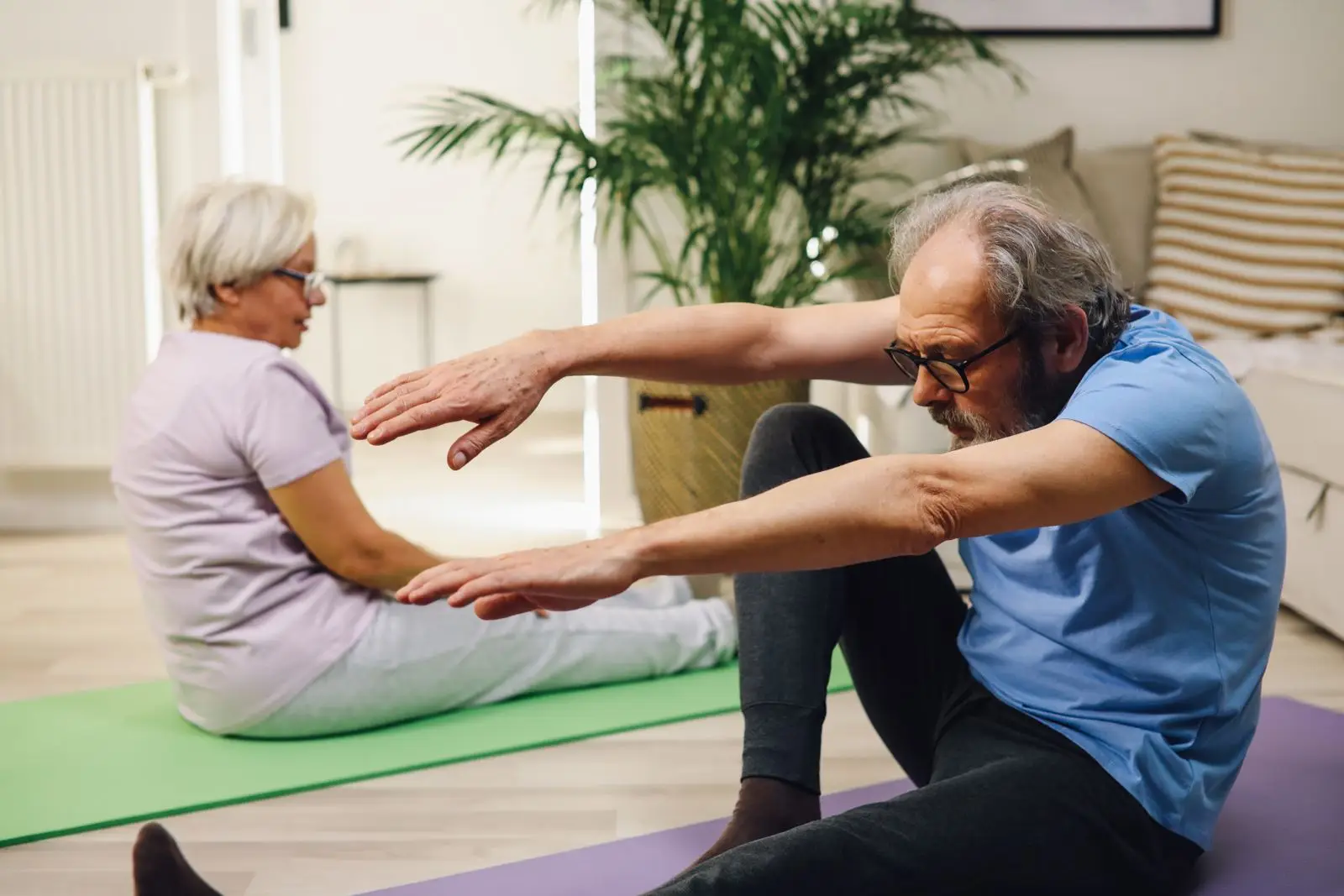 Un couple âgé faisant des étirements doux ensemble dans un salon lumineux.