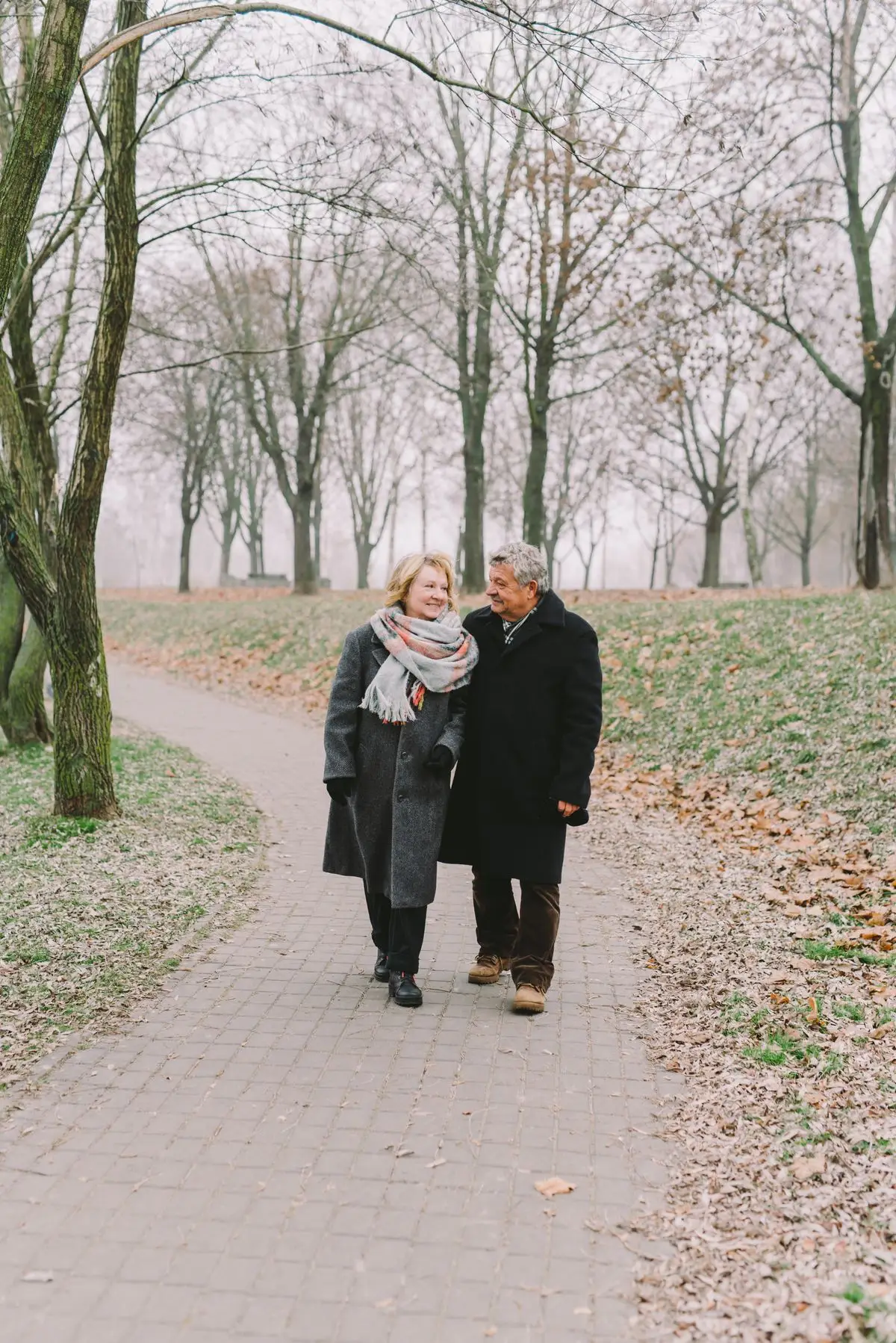 Un couple âgé marchant bras dessus bras dessous le long d'un chemin bordé d'arbres dans la douce lumière du matin.